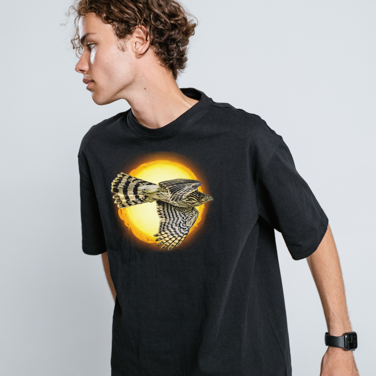 Person wearing a black t-shirt with a hawk design on a plain background